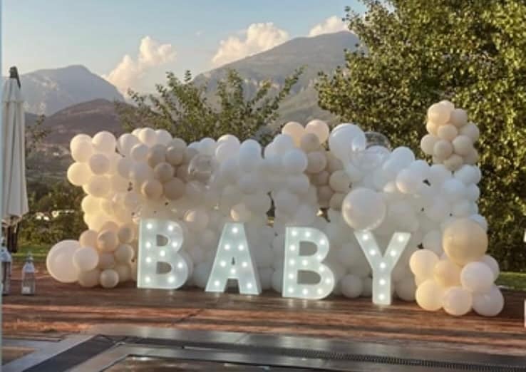 Baby shower: white balloons around light-up letters spelling BABY, mountains behind