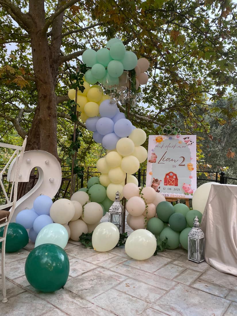 Second birthday setup with sage, cream and yellow balloons and a light-up 2