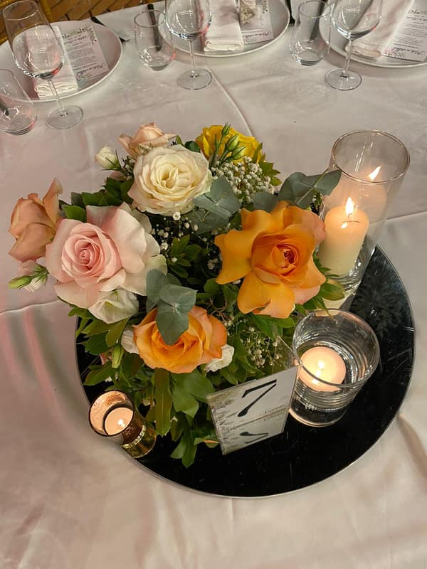 Centrepiece of peach and white roses with candles on a black charger