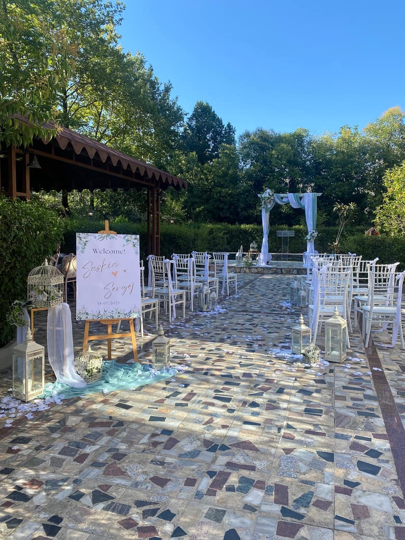 The finished ceremony: rows of white chairs, a welcome sign and lanterns along a stone aisle towards a draped arch