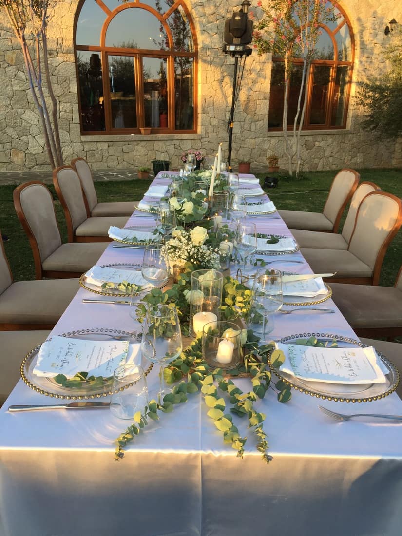 Long table in a stone courtyard with a garland of white flowers and candles