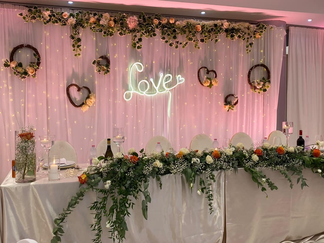 Pink backdrop with a 'Love' neon sign and a flower garland
