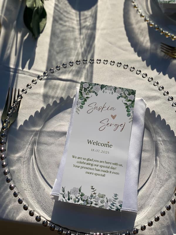 Printed welcome card with greenery on a silver charger plate