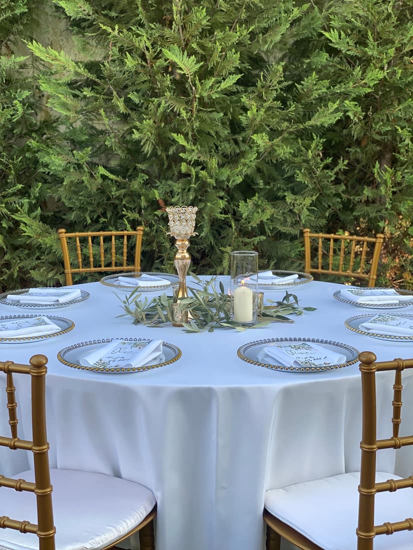 Round table with white cloth, gold chairs and a centrepiece
